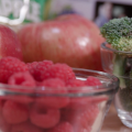 A display of produce including red raspberries in a small clear glass bowl, green broccoli florets in a small clear glass bowl, 2 red apples behind the bowls. Does that work? 