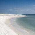 Dark blue water meets the edge of white sand on a clean, empty beach.