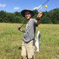 A teenage boy proudly holds up a catfish on his fishing line.