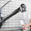 Water flows from a stainless steel kitchen faucet into a clear drinking glass.