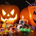 Orange pumpkins and a carved jack-o-lantern sit on a table behind a smiling ceramic jack-o-lantern candy dish. Toys, candy and candles are displayed in front of the pumpkins.