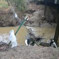 A drainage ditch with moving water, limbs, and trash.