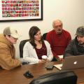 A group of three students gather around a computer while a man looks on from behind.