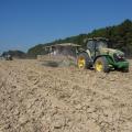 Two tractors pull harvest carts across a dusty field.