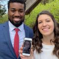 A smiling couple holds a smart phone showing a woman on a video call.