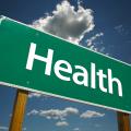 A green road sign with the word “Health” is pictured against a blue sky with white clouds.