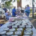 Rows of canning jars line a table at an open-air marketplace.