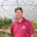 Man in a maroon shirt and baseball cap in a greenhouse.