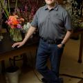 A man stands at a table holding floral arrangements.