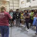 A man shows a Van de Graaff generator to students on a class trip.	