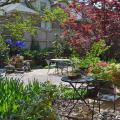 Tables and chairs are on a patio in a backyard garden.