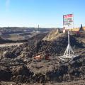 Wide shot of a surface coal mine featuring a layered landscape of exposed rock and soil, heavy machinery, and a sign that reads “caution, entering work area channel.