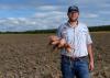 A man stands in a field with sweet potatoes in his hand.