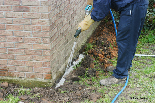 Liquid termiticide is being applied to the exterior perimeter of this house to establish a treated soil barrier that will prevent termite attack.