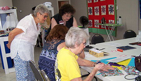 Two standing, clothing volunteers observe another volunteer as show works at a table.