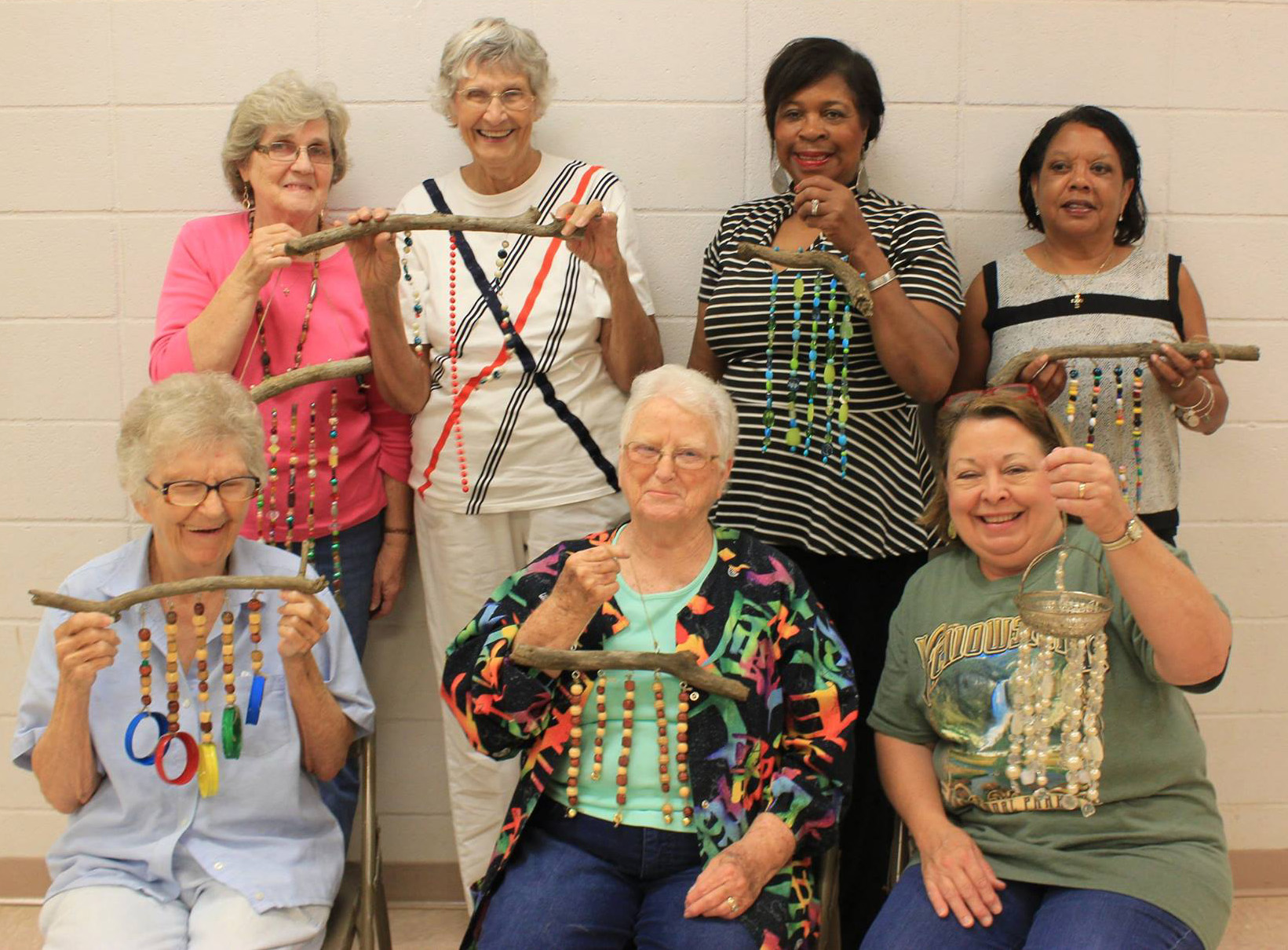 Seven women smile as they hold beaded windchimes.